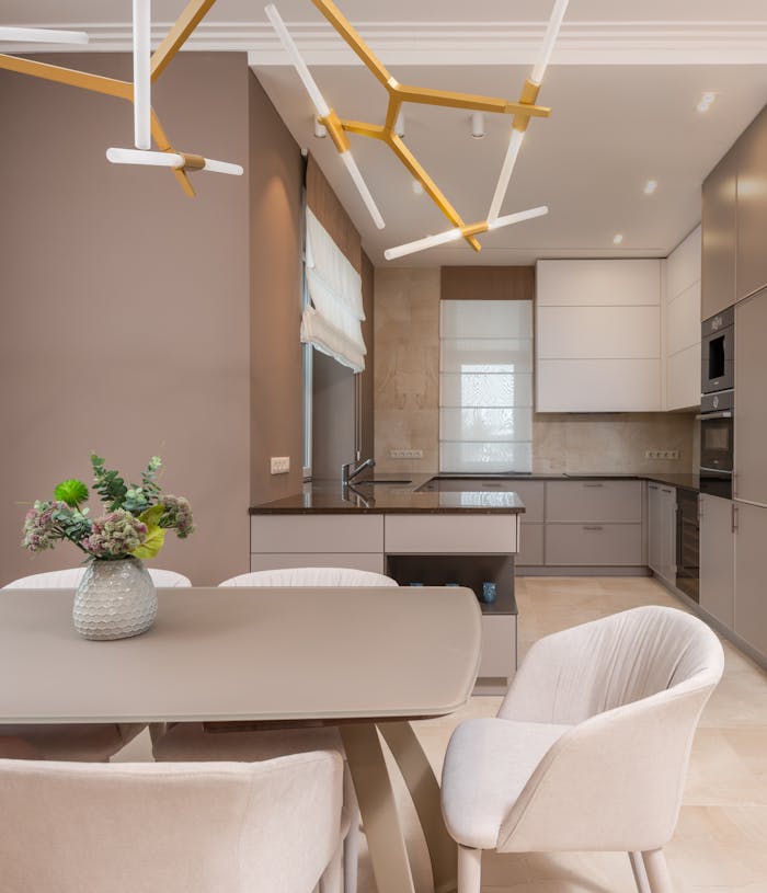 About A stylish, open-plan kitchen and dining area featuring neutral tones, modern furniture, and elegant lighting.