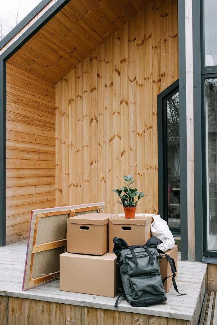 A modern wooden home exterior with moving boxes and potted plant on a sunny day.